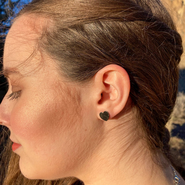 A side view of a girl wearing small silver-colored heart stud earrings