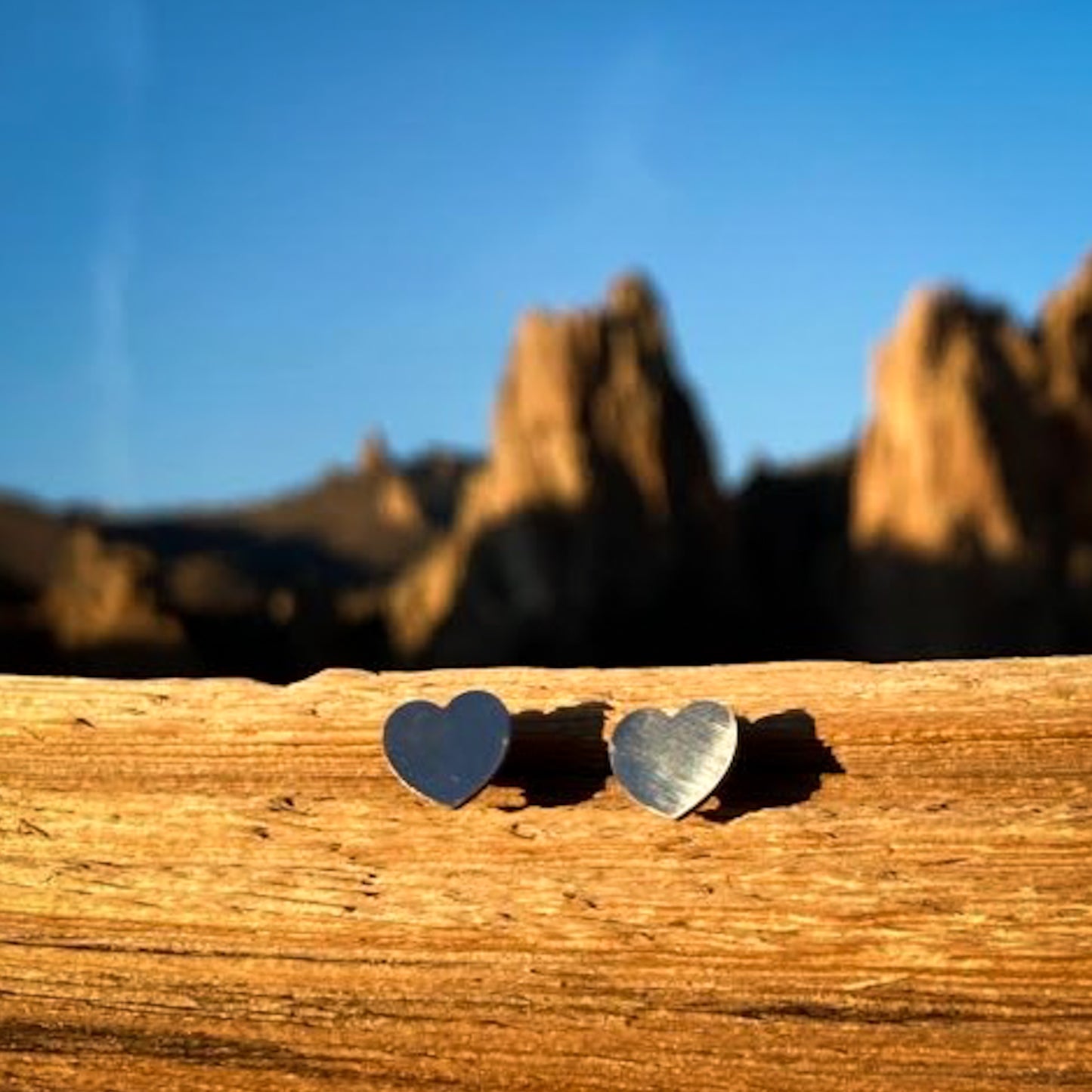 Small silver-colored heart stud earrings with a mountain in the background